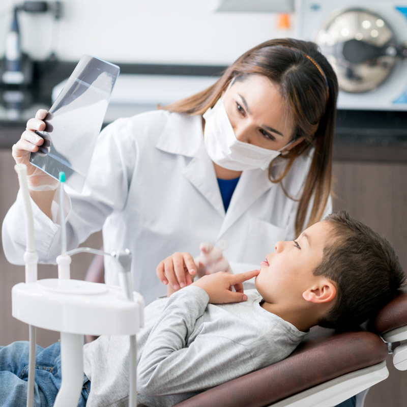 Happy dentist looking at an x-ray with his young patient at the office